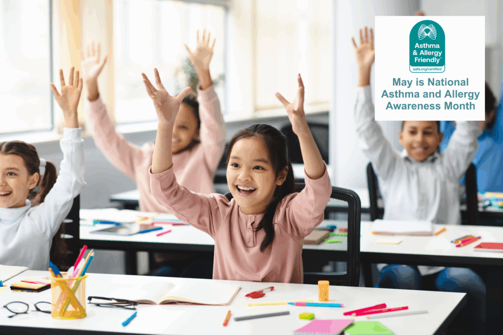 Children smiling and raising their hands in a bright, modern classroom. A badge reads “May is National Asthma and Allergy Awareness Month” from the Asthma & Allergy Friendly® Certification Program. Indoor air quality in schools