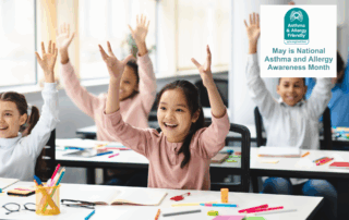 Children smiling and raising their hands in a bright, modern classroom. A badge reads “May is National Asthma and Allergy Awareness Month” from the Asthma & Allergy Friendly® Certification Program. Indoor air quality in schools